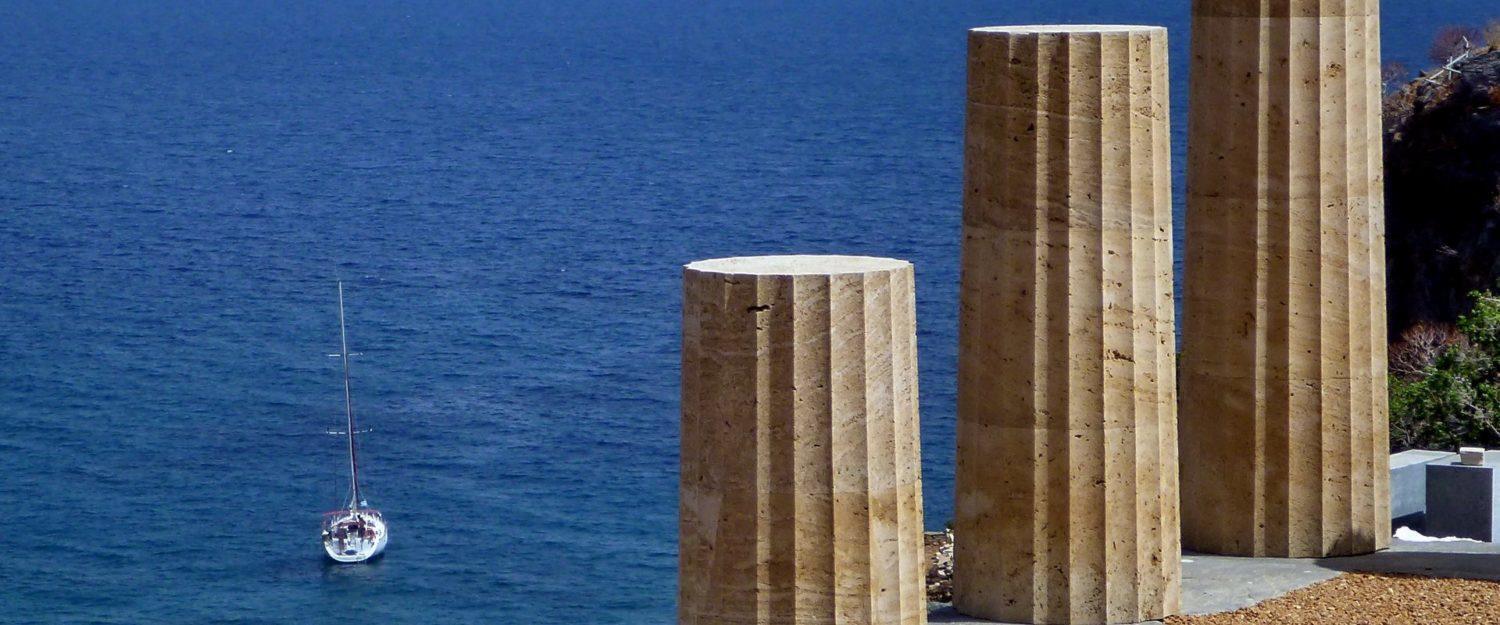 Ancient Greek ruins overlooking the sea, with a skippered yacht charter anchored nearby, blending history and adventure.
