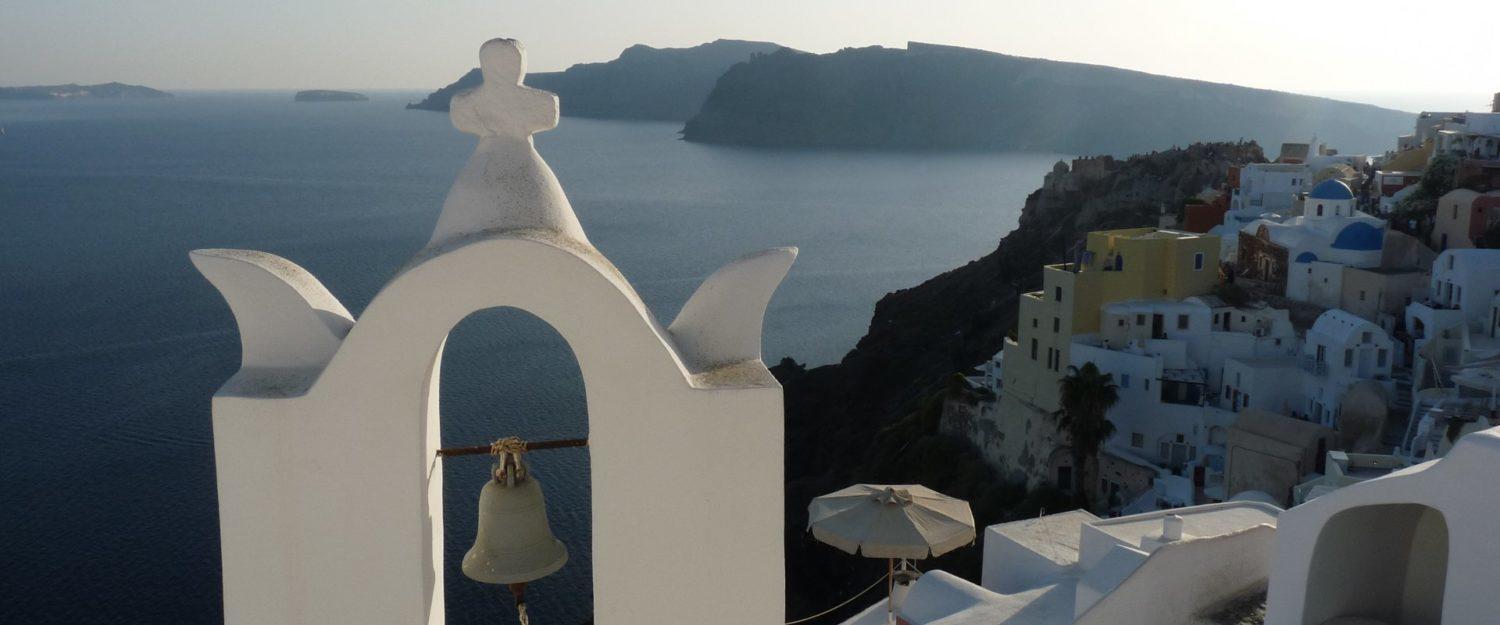 A traditional white church bell tower overlooking the Aegean Sea in Santorini, Greece, with stunning caldera views and whitewashed buildings in the background