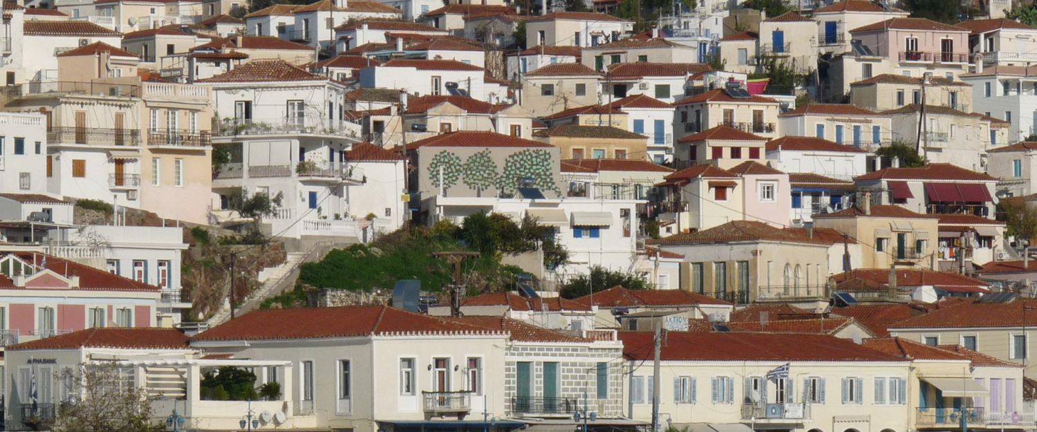 A panoramic view of a classic Greek island town with white houses and red rooftops, seen from a skippered yacht charter