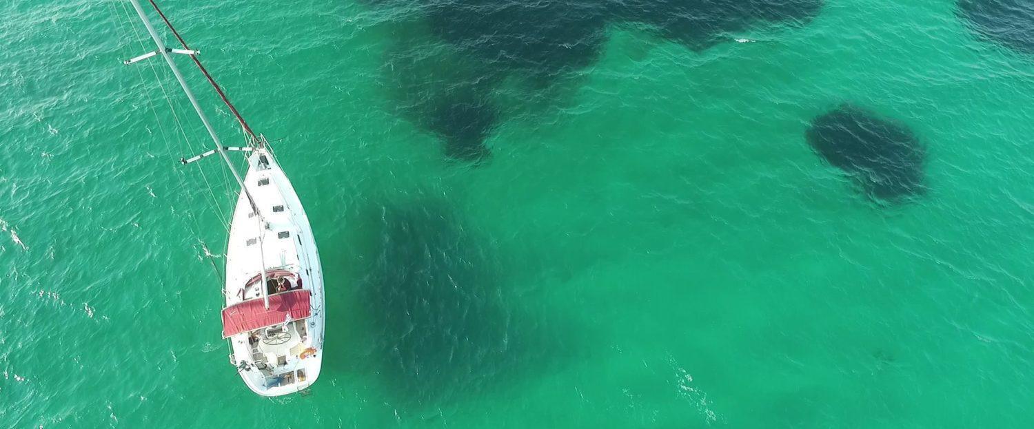 An aerial view of a skippered yacht charter anchored in turquoise waters, surrounded by beautiful underwater reefs