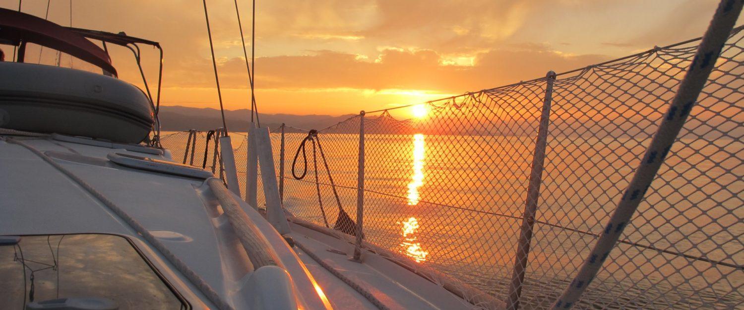 Golden sunset over the sea from the deck of a skippered yacht charter in Greece, creating a breathtaking sailing experience