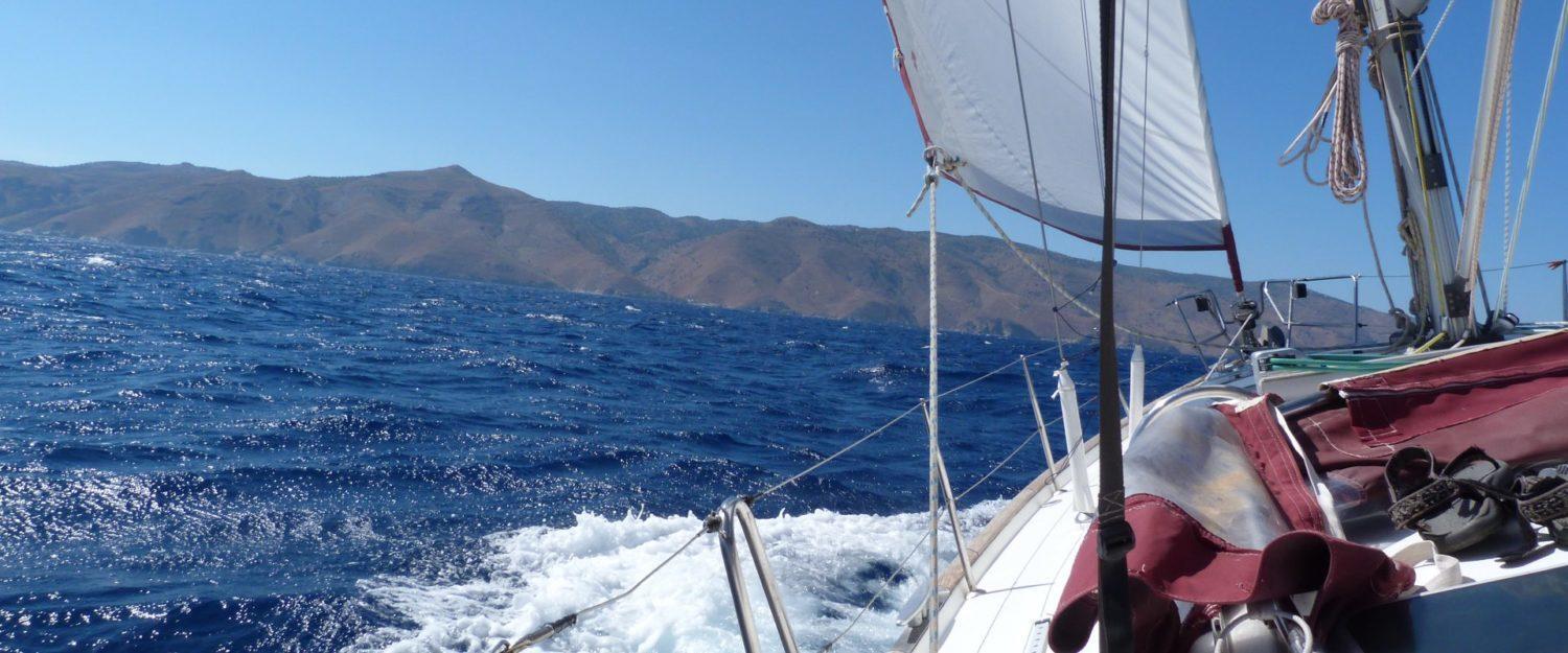 Sailing through the deep blue waters with a view of rugged Greek island landscapes from a skippered yacht charter